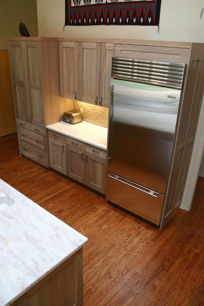 Cette photo montre une cuisine ouverte chic en L avec un évier intégré, un placard avec porte à panneau encastré, des portes de placard grises, une crédence beige, un électroménager en acier inoxydable, un sol en bois brun et îlot.