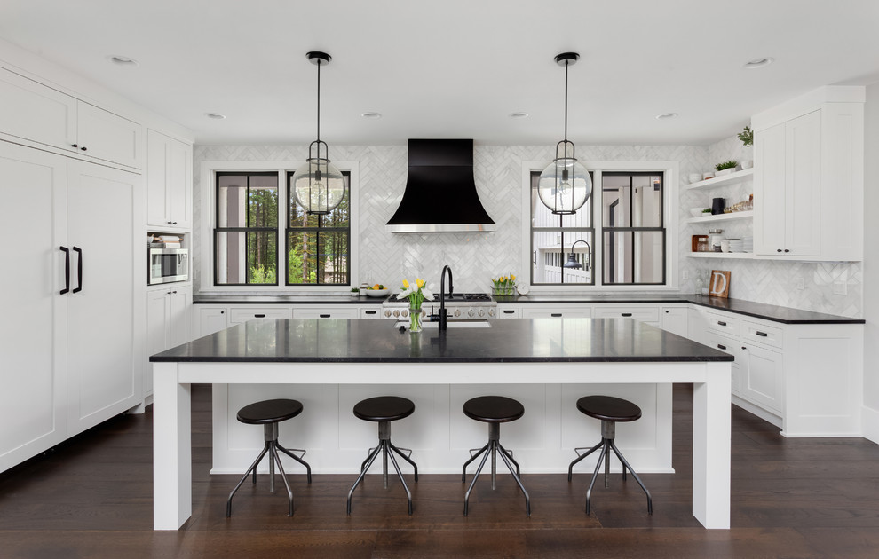 This is an example of a medium sized contemporary u-shaped kitchen/diner in DC Metro with a belfast sink, beaded cabinets, white cabinets, engineered stone countertops, white splashback, marble splashback, stainless steel appliances, dark hardwood flooring, an island, brown floors and black worktops.