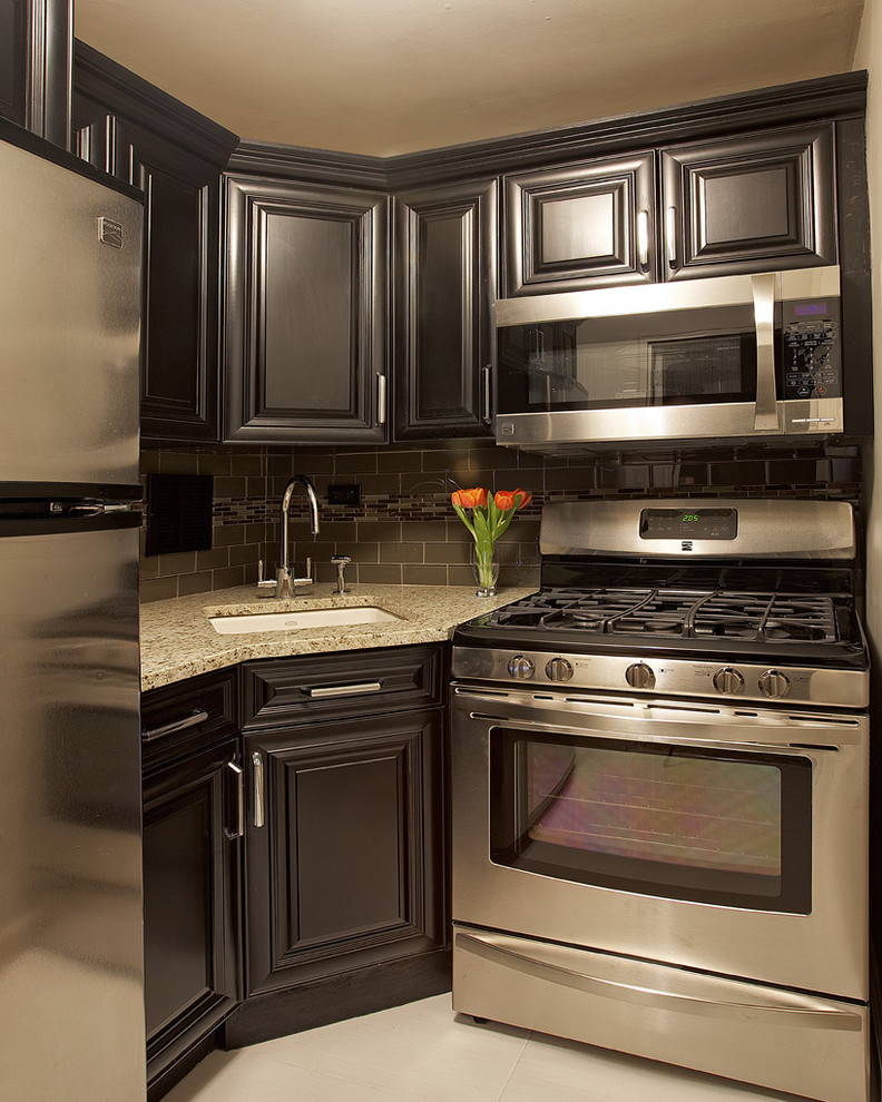 Elegant kitchen photo in New York with an undermount sink, raised-panel cabinets, black cabinets, gray backsplash, subway tile backsplash and stainless steel appliances