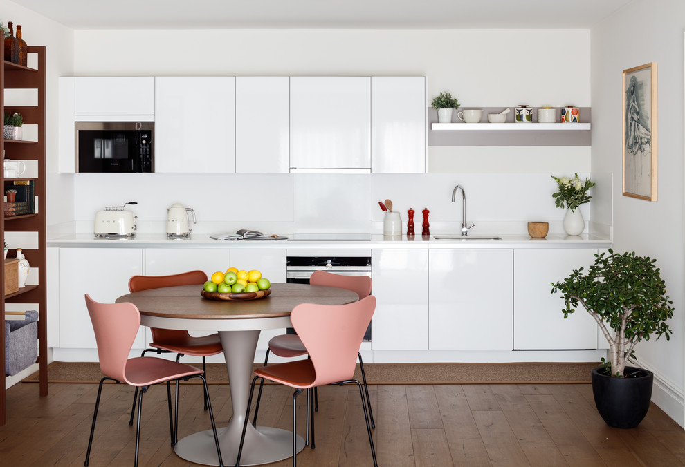 Inredning av ett modernt vit linjärt vitt kök och matrum, med en undermonterad diskho, släta luckor, vita skåp, rostfria vitvaror, mörkt trägolv och brunt golv