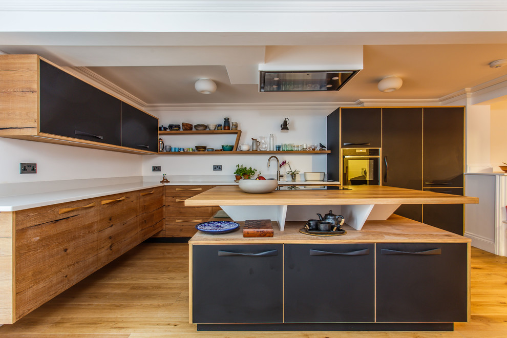 This is an example of a medium sized modern l-shaped kitchen in Sussex with a submerged sink, flat-panel cabinets, medium wood cabinets, stainless steel appliances, light hardwood flooring, an island, beige floors, white worktops and wood worktops.