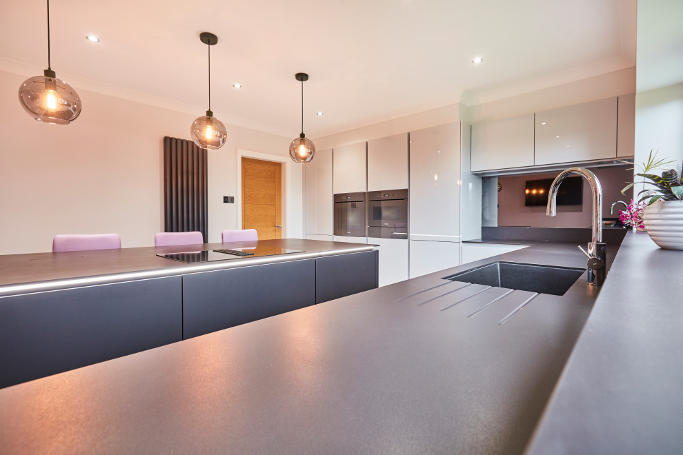 Inspiration for a medium sized contemporary l-shaped kitchen/diner in Other with a submerged sink, flat-panel cabinets, white cabinets, black appliances, an island, grey floors, grey worktops, limestone worktops, metallic splashback, mirror splashback, porcelain flooring and a coffered ceiling.
