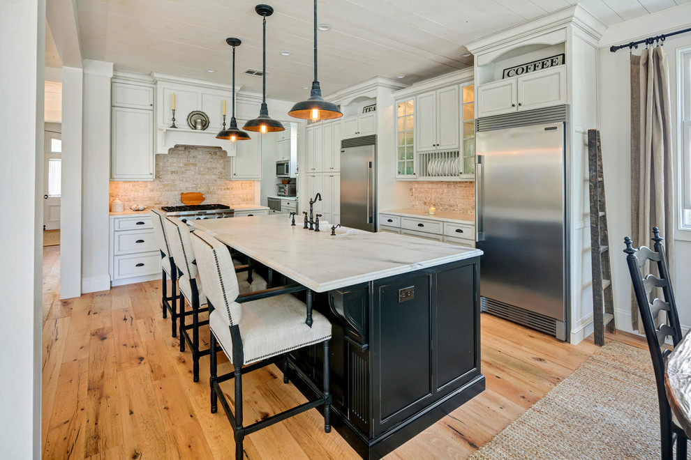 Rustik inredning av ett kök, med en rustik diskho, luckor med infälld panel, svarta skåp, marmorbänkskiva, flerfärgad stänkskydd, rostfria vitvaror, ljust trägolv och en köksö