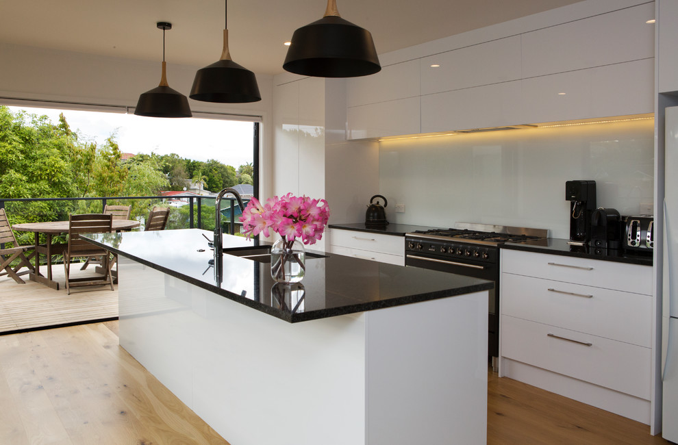 Photo of a medium sized contemporary galley kitchen/diner in Auckland with a double-bowl sink, white cabinets, granite worktops, blue splashback, glass sheet splashback, black appliances, laminate floors, an island and yellow floors.