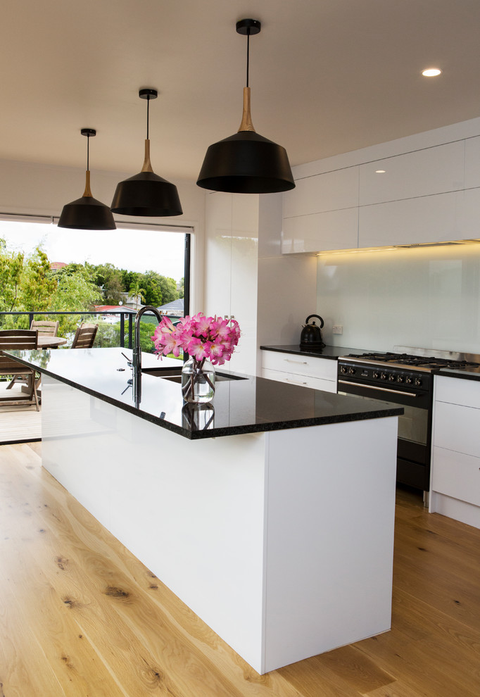 Mid-sized trendy galley laminate floor and yellow floor eat-in kitchen photo in Auckland with a double-bowl sink, white cabinets, granite countertops, blue backsplash, glass sheet backsplash, black appliances and an island