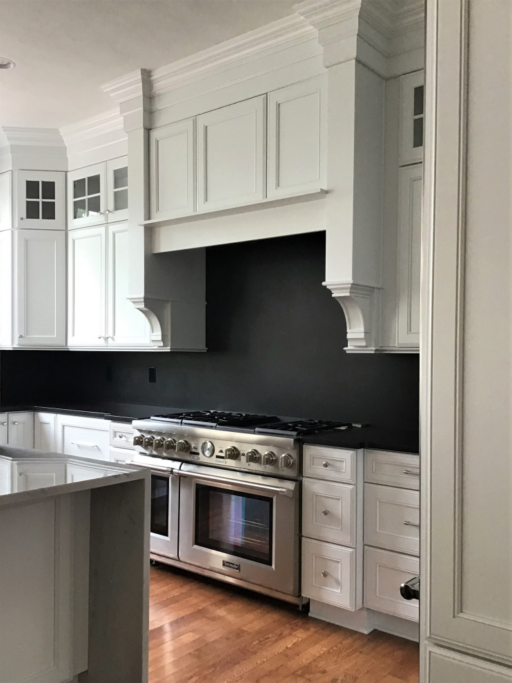 Large transitional u-shaped medium tone wood floor and brown floor eat-in kitchen photo in Other with a farmhouse sink, flat-panel cabinets, white cabinets, quartzite countertops, black backsplash, stone slab backsplash, stainless steel appliances, an island and black countertops