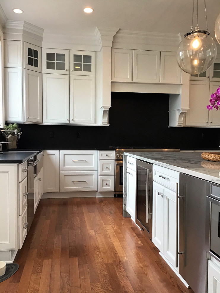 Large transitional u-shaped medium tone wood floor and brown floor eat-in kitchen photo in Other with a farmhouse sink, flat-panel cabinets, white cabinets, quartzite countertops, black backsplash, stone slab backsplash, stainless steel appliances, an island and black countertops
