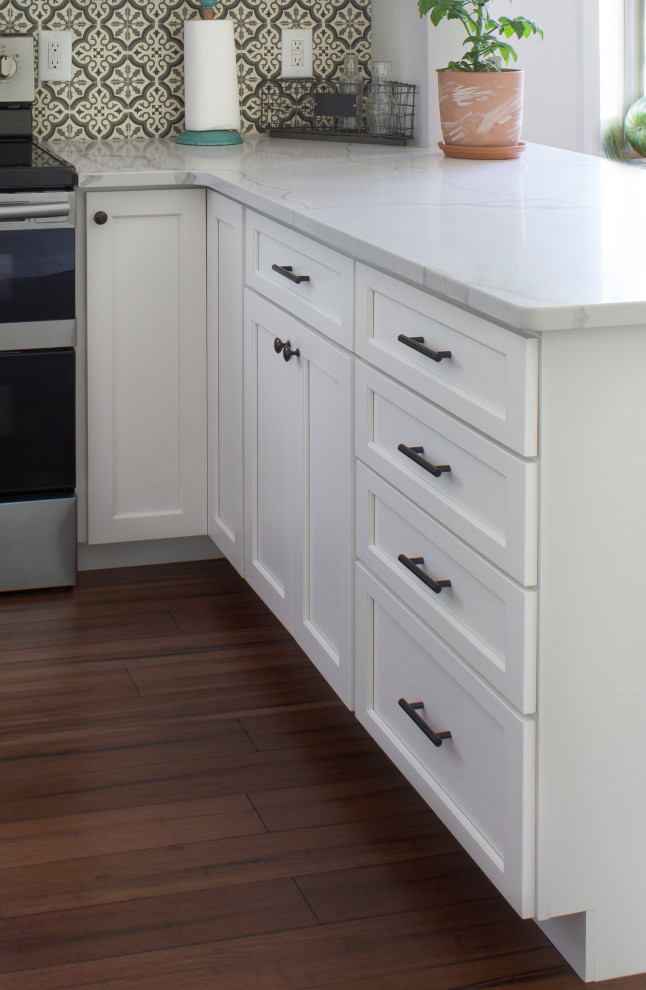 ニューヨークにある小さなトラディショナルスタイルのおしゃれなキッチン (ダブルシンク、シェーカースタイル扉のキャビネット、白いキャビネット、御影石カウンター、マルチカラーのキッチンパネル、セラミックタイルのキッチンパネル、黒い調理設備、ラミネートの床、茶色い床、白いキッチンカウンター) の写真
