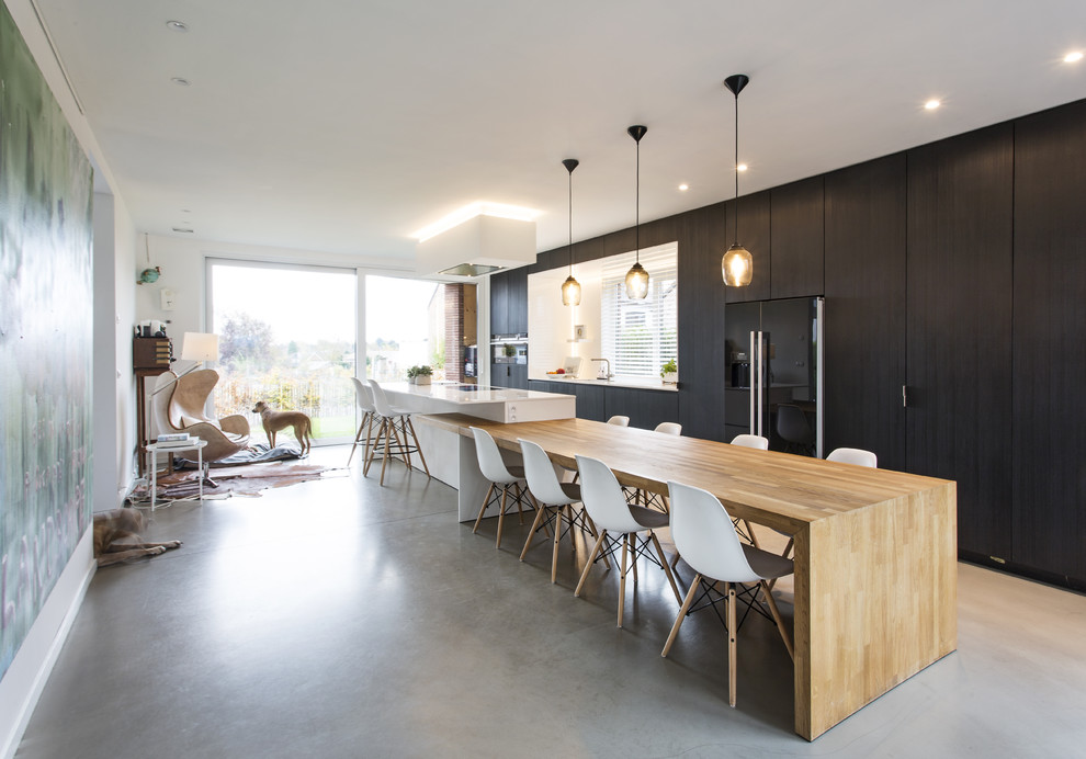 Large contemporary galley kitchen/diner in DC Metro with a submerged sink, flat-panel cabinets, black cabinets, quartz worktops, black appliances, concrete flooring, an island, beige floors and white worktops.
