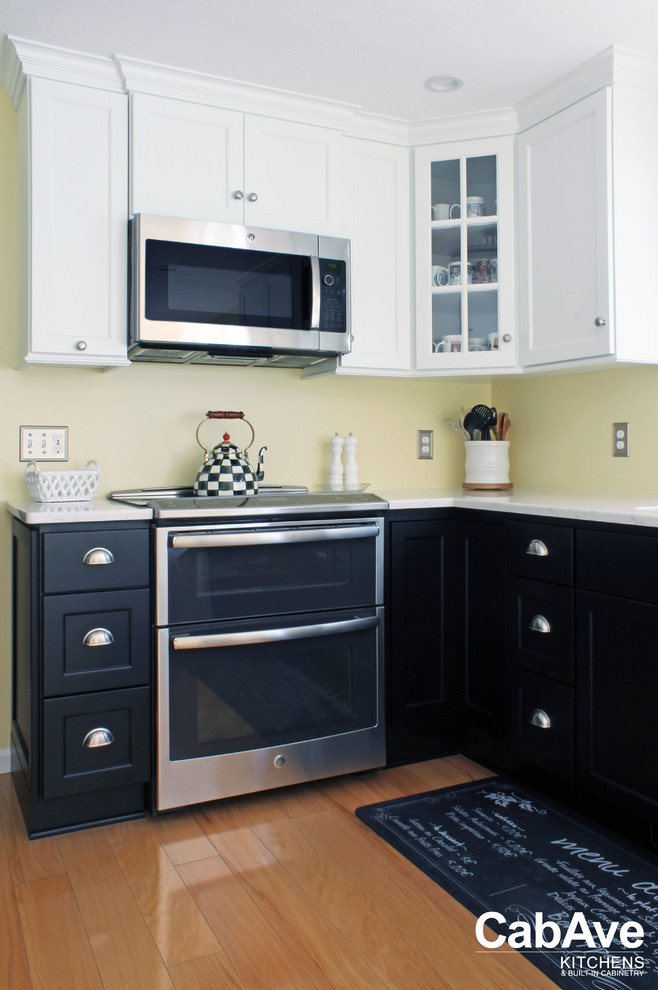 Bild på ett litet vintage kök, med en undermonterad diskho, luckor med infälld panel, svarta skåp, bänkskiva i kvarts, gult stänkskydd, rostfria vitvaror, mellanmörkt trägolv, en halv köksö och brunt golv