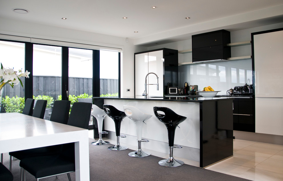 Bild på ett mellanstort funkis kök, med en undermonterad diskho, svarta skåp, granitbänkskiva, grått stänkskydd, glaspanel som stänkskydd, rostfria vitvaror, klinkergolv i porslin, en köksö och vitt golv