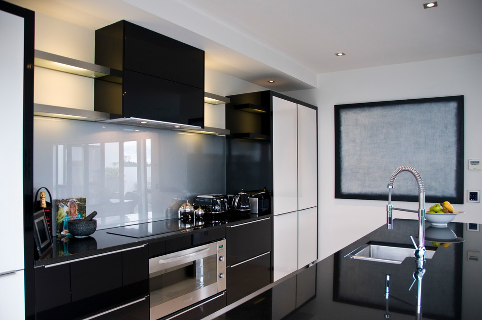 Inspiration för ett mellanstort funkis kök, med en undermonterad diskho, svarta skåp, granitbänkskiva, grått stänkskydd, glaspanel som stänkskydd, rostfria vitvaror, klinkergolv i porslin, en köksö och vitt golv