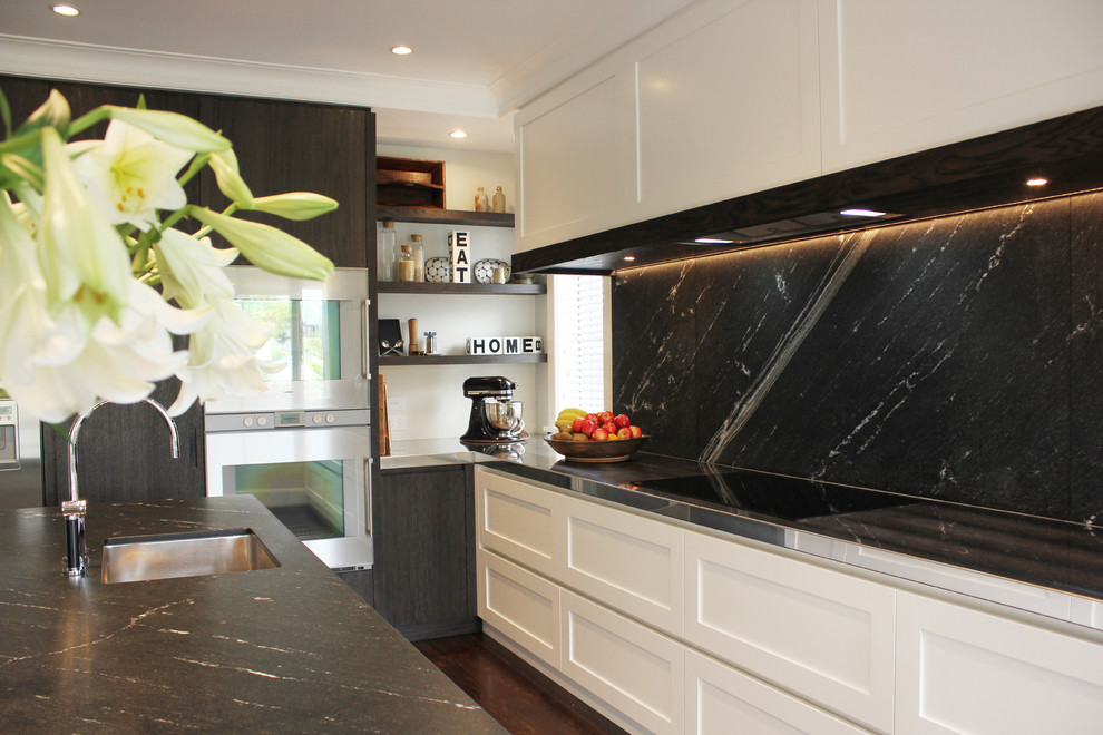 Photo of a contemporary kitchen in Auckland with shaker cabinets, white cabinets, black splashback and stainless steel appliances.