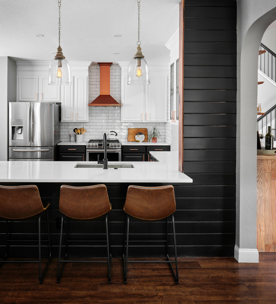 Mid-sized transitional u-shaped medium tone wood floor and brown floor kitchen photo in Austin with an undermount sink, raised-panel cabinets, quartz countertops, white backsplash, subway tile backsplash, stainless steel appliances, white countertops, black cabinets and a peninsula