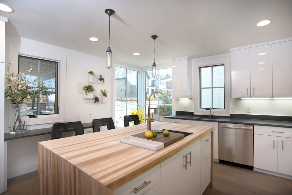 Exempel på ett modernt kök, med en enkel diskho, släta luckor, vita skåp, träbänkskiva, svart stänkskydd, stänkskydd i sten, rostfria vitvaror, ljust trägolv och en köksö