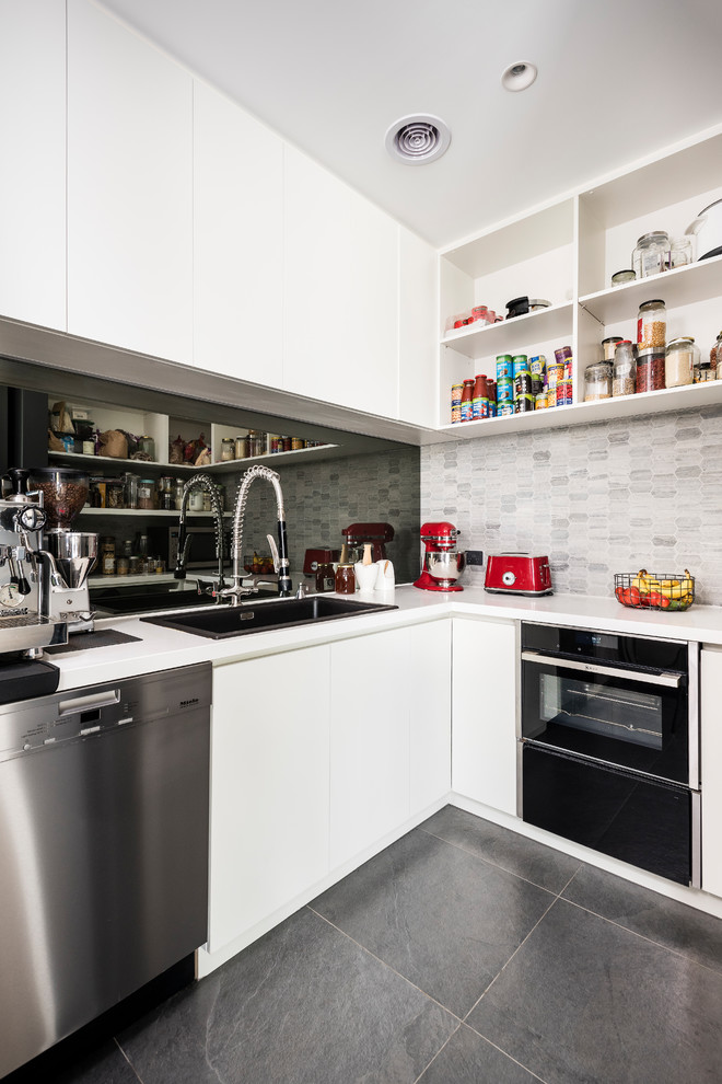 Bild på ett stort funkis vit vitt kök, med en undermonterad diskho, släta luckor, svarta skåp, bänkskiva i kvarts, vitt stänkskydd, glaspanel som stänkskydd, rostfria vitvaror, klinkergolv i porslin, en köksö och grått golv