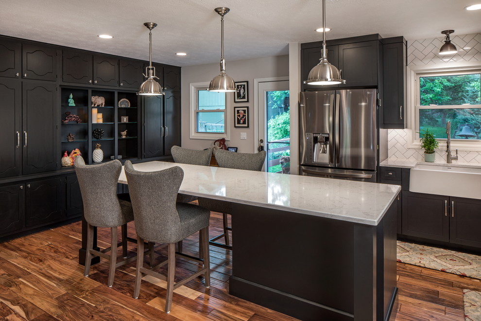 Eat-in kitchen - mid-sized transitional l-shaped dark wood floor and brown floor eat-in kitchen idea in Omaha with black cabinets, quartz countertops, a farmhouse sink, shaker cabinets, white backsplash, subway tile backsplash, stainless steel appliances and an island