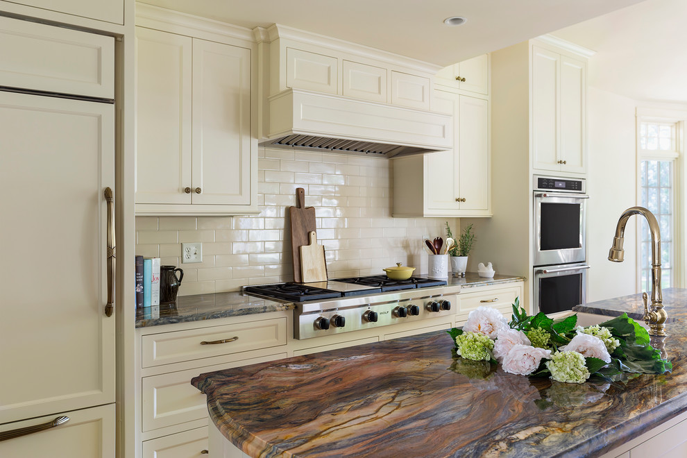 ミネアポリスにある広いトラディショナルスタイルのおしゃれなアイランドキッチン (エプロンフロントシンク、落し込みパネル扉のキャビネット、白いキャビネット、珪岩カウンター、白いキッチンパネル、サブウェイタイルのキッチンパネル、パネルと同色の調理設備、淡色無垢フローリング、茶色い床、マルチカラーのキッチンカウンター) の写真