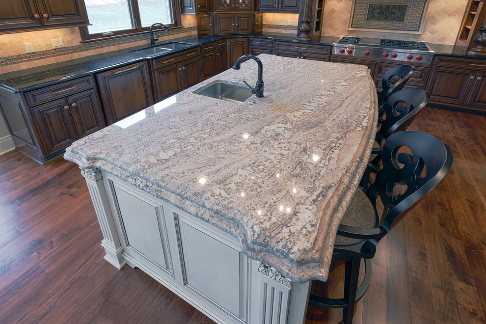 Cette image montre une cuisine traditionnelle avec un plan de travail en granite, une crédence beige, une crédence en carrelage de pierre et un sol en bois brun.