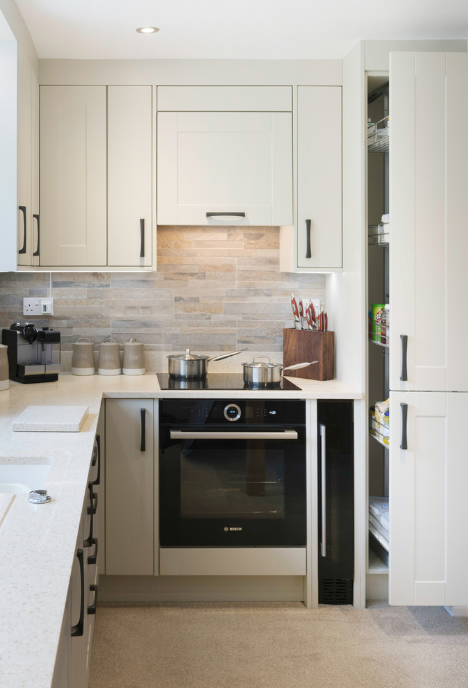 This is an example of a small traditional l-shaped enclosed kitchen in Cornwall with a belfast sink, shaker cabinets, granite worktops, grey splashback, stone slab splashback, black appliances and beige worktops.