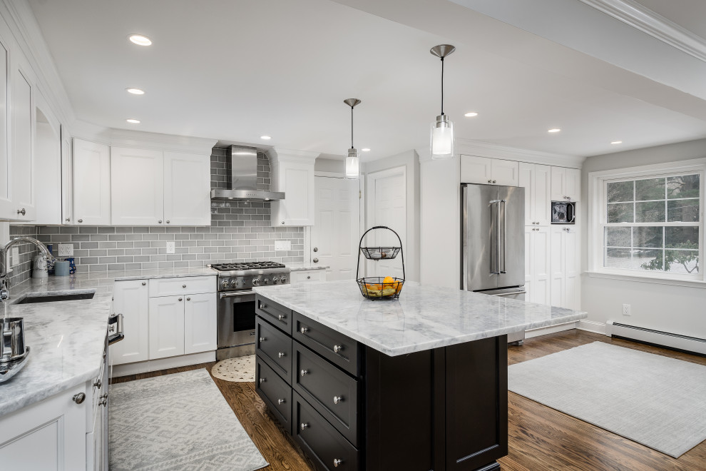 This is an example of a large traditional l-shaped kitchen/diner in Philadelphia with a built-in sink, shaker cabinets, white cabinets, engineered stone countertops, grey splashback, porcelain splashback, stainless steel appliances, medium hardwood flooring, an island, brown floors and grey worktops.