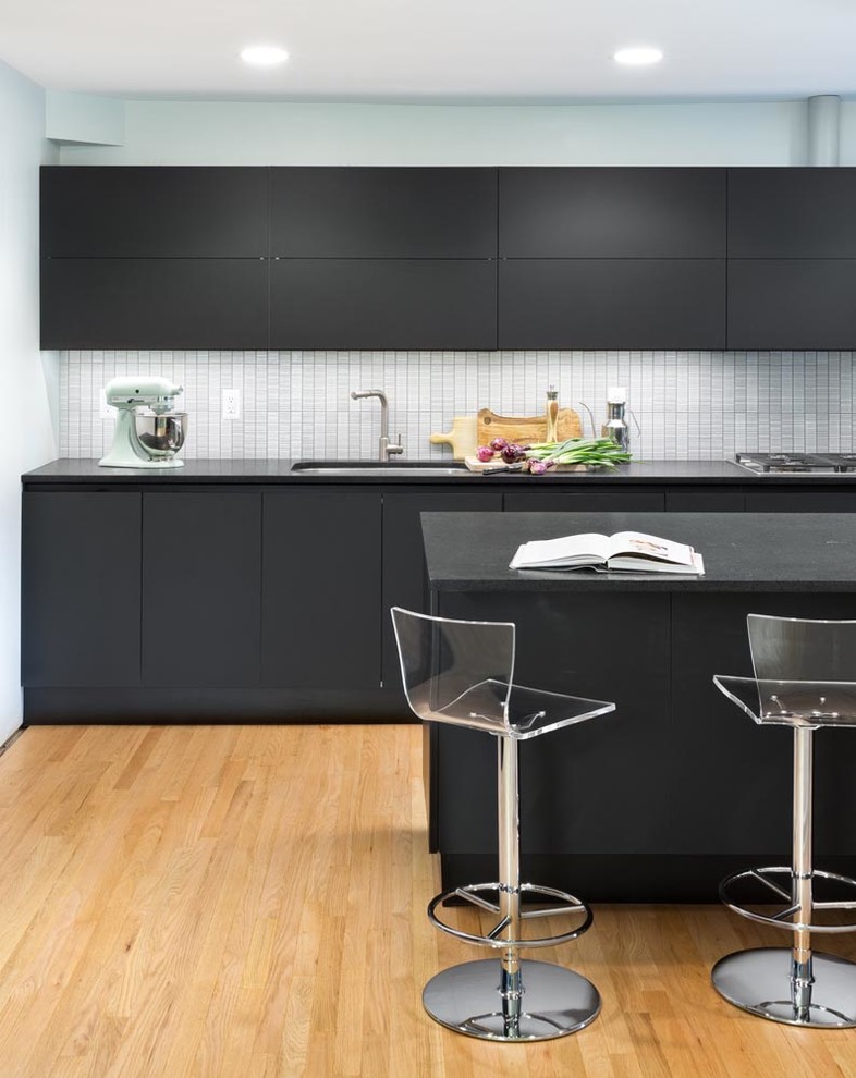 Inspiration for a contemporary light wood floor eat-in kitchen remodel in Chicago with an undermount sink, glass-front cabinets, black cabinets, granite countertops, white backsplash, ceramic backsplash, paneled appliances and an island