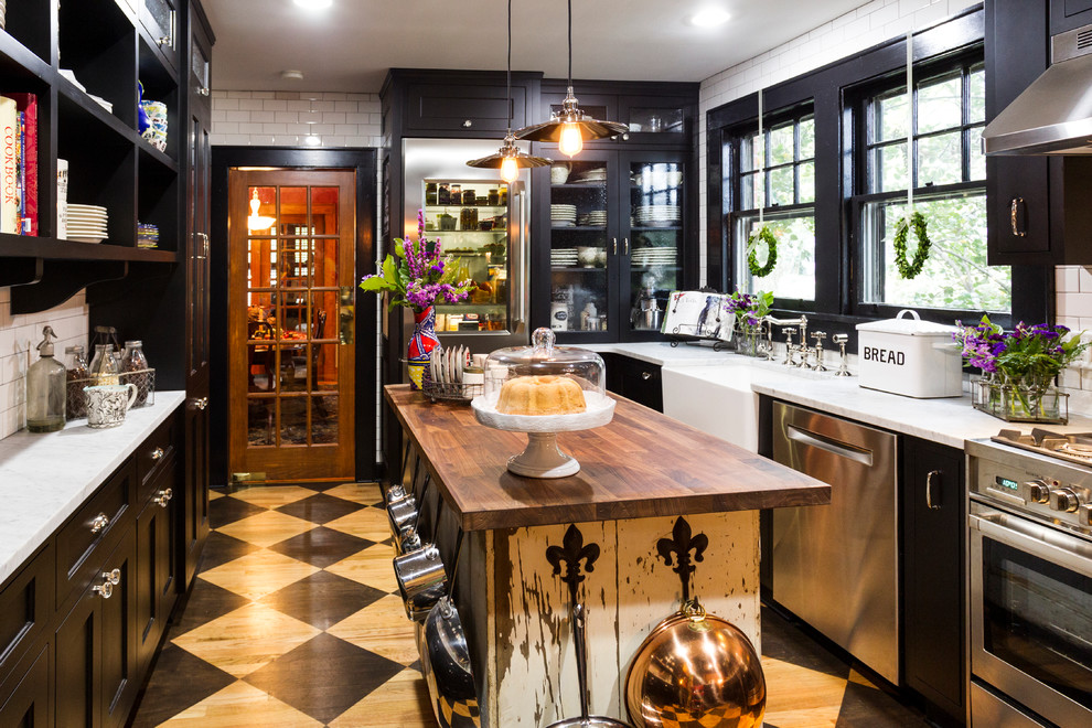 Example of a mid-sized classic painted wood floor and black floor enclosed kitchen design in Charlotte with a farmhouse sink, black cabinets, marble countertops, white backsplash, subway tile backsplash, stainless steel appliances, an island and shaker cabinets