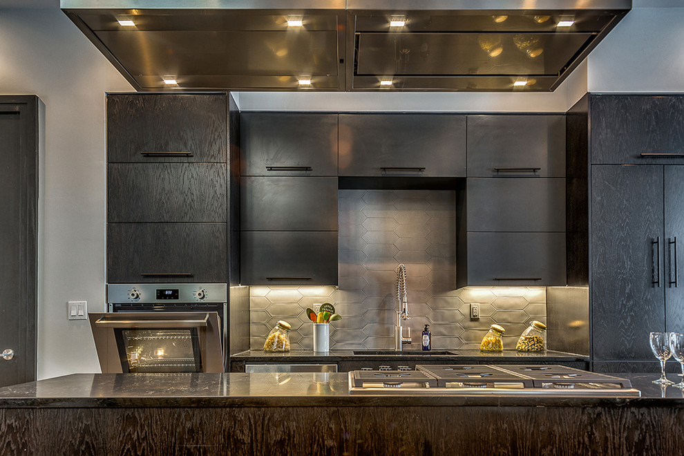 ニューヨークにあるコンテンポラリースタイルのおしゃれなアイランドキッチン (シングルシンク、フラットパネル扉のキャビネット、黒いキャビネット、ステンレスカウンター、グレーのキッチンパネル、シルバーの調理設備) の写真