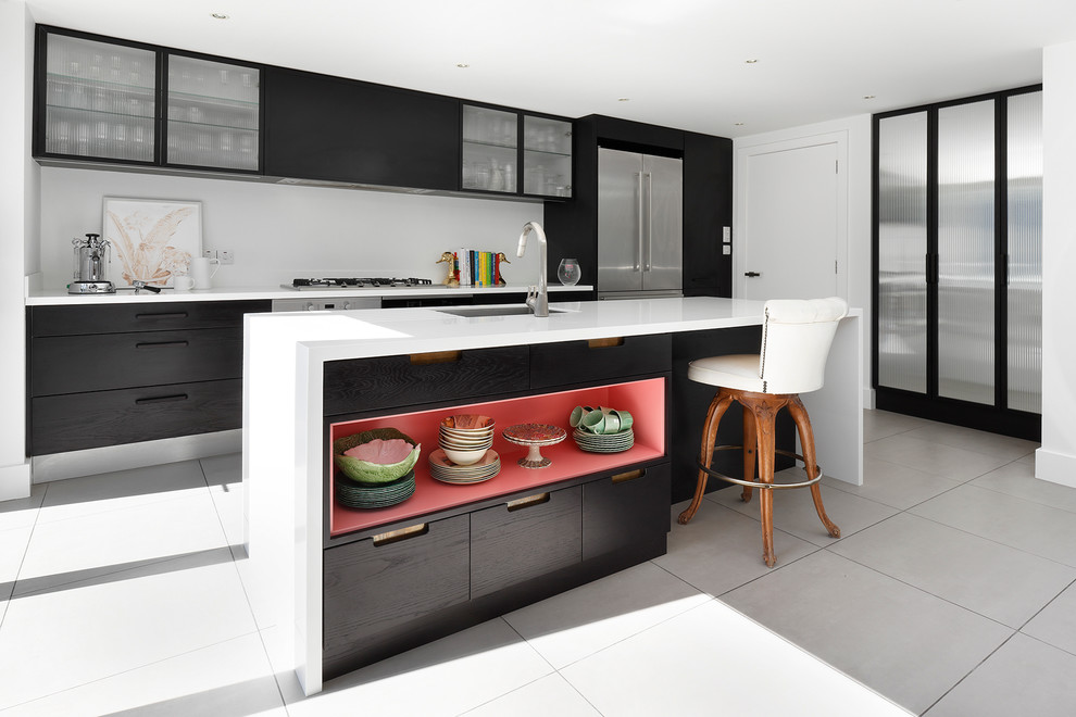 Contemporary galley enclosed kitchen in London with a submerged sink, glass-front cabinets, white splashback, stainless steel appliances and an island.