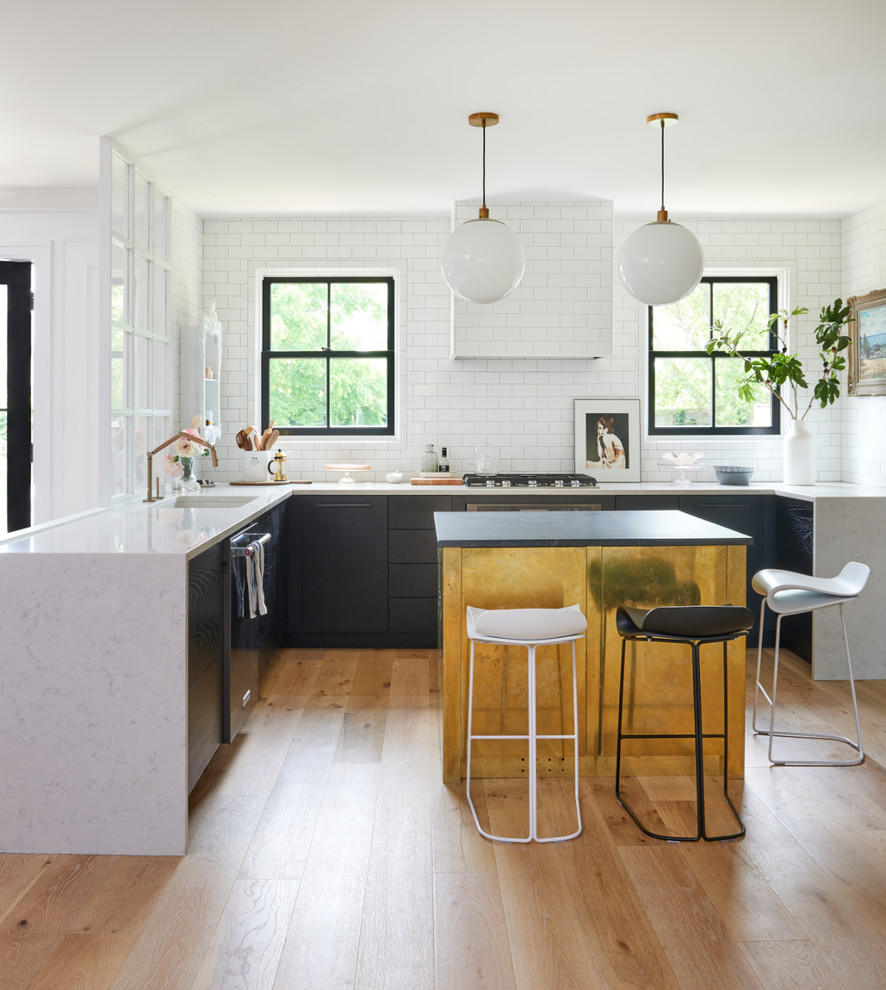 Photo of a contemporary u-shaped kitchen in Other with a single-bowl sink, flat-panel cabinets, white splashback, metro tiled splashback, light hardwood flooring, an island, beige floors and white worktops.