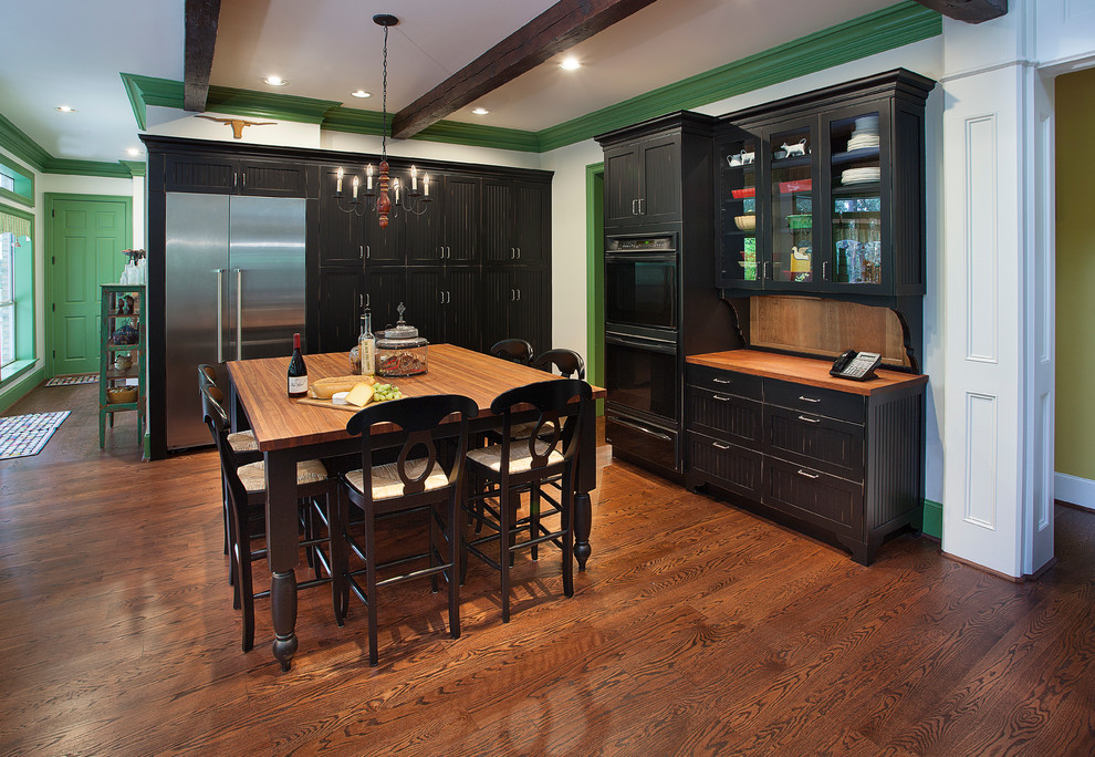 Example of a large country l-shaped medium tone wood floor open concept kitchen design in Houston with shaker cabinets, black cabinets, wood countertops, black appliances, two islands and an undermount sink