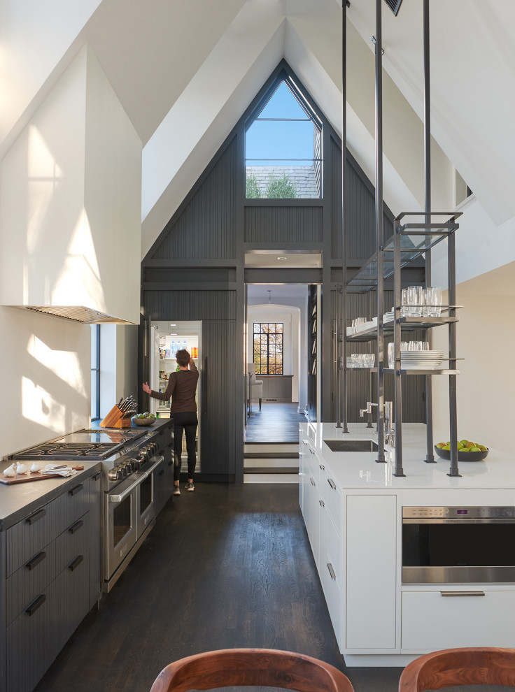 Large modern galley kitchen/diner in DC Metro with a single-bowl sink, glass-front cabinets, black cabinets, engineered stone countertops, white splashback, black appliances, dark hardwood flooring, an island, black floors and white worktops.