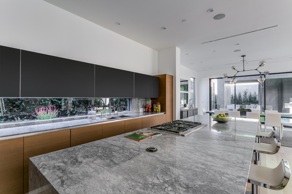 Modern inredning av ett kök, med en dubbel diskho, släta luckor, svarta skåp, marmorbänkskiva, flerfärgad stänkskydd, rostfria vitvaror, mellanmörkt trägolv och en köksö