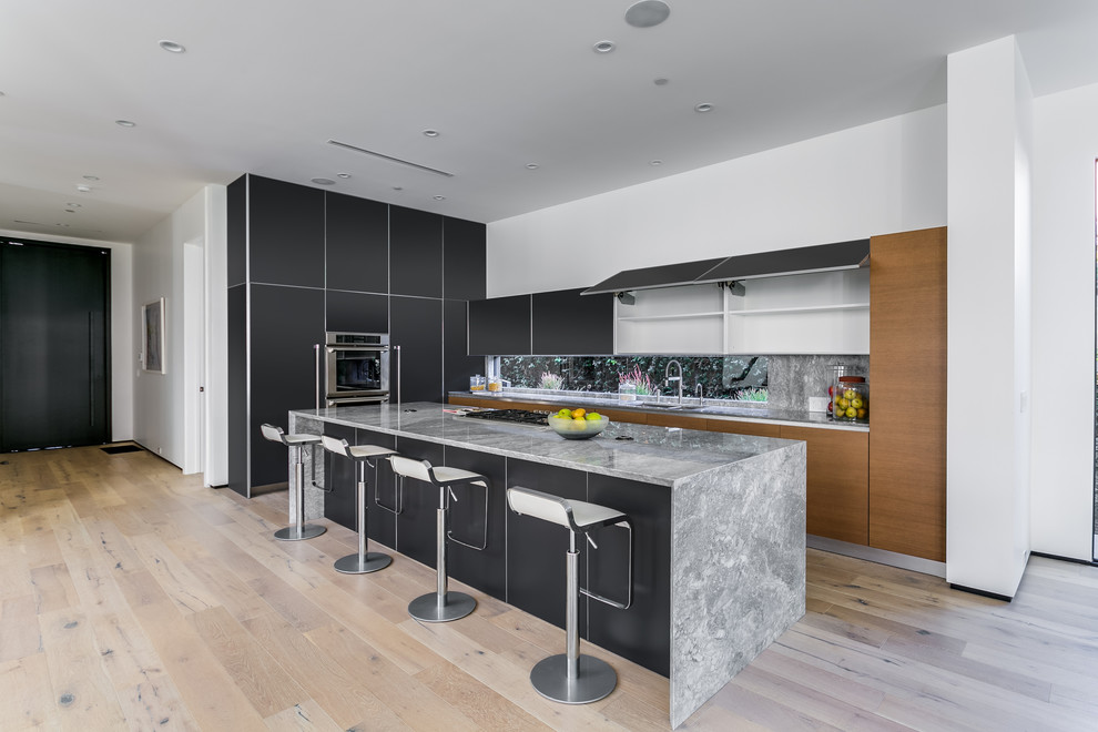 Trendy l-shaped medium tone wood floor open concept kitchen photo in Los Angeles with a double-bowl sink, flat-panel cabinets, black cabinets, marble countertops, multicolored backsplash, stainless steel appliances and an island