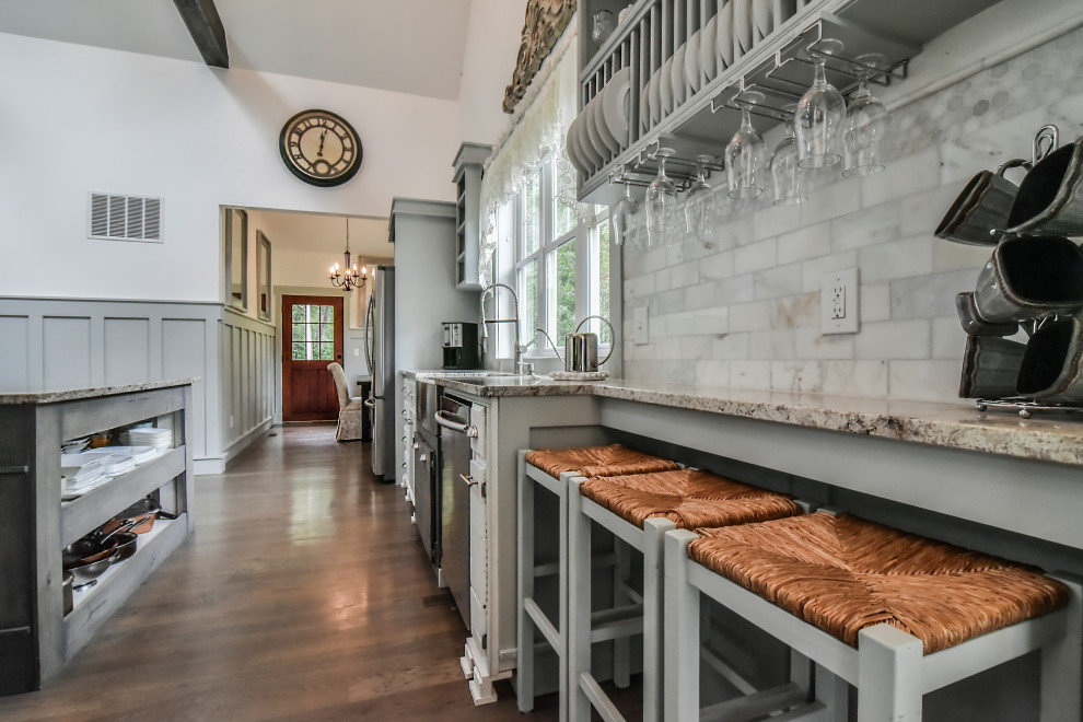 Example of a mid-sized arts and crafts light wood floor and gray floor eat-in kitchen design in Other with a farmhouse sink, raised-panel cabinets, white cabinets, granite countertops, white backsplash, marble backsplash, stainless steel appliances, an island and multicolored countertops