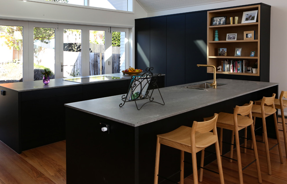 Photo of a large contemporary galley kitchen/diner in Auckland with a submerged sink, black cabinets, engineered stone countertops, grey splashback, stone tiled splashback, stainless steel appliances, medium hardwood flooring, multiple islands, brown floors and grey worktops.