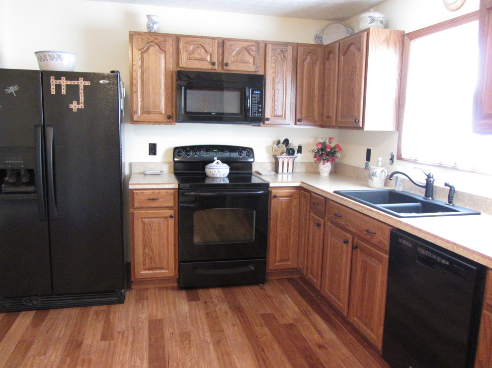 Example of a classic l-shaped light wood floor kitchen design in Columbus with a double-bowl sink, light wood cabinets, laminate countertops and black appliances