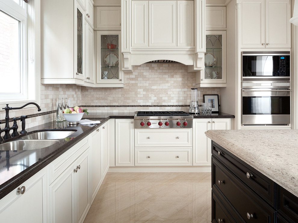 Exempel på ett stort klassiskt l-kök, med en dubbel diskho, luckor med infälld panel, vita skåp, beige stänkskydd, rostfria vitvaror, en köksö och stänkskydd i stenkakel