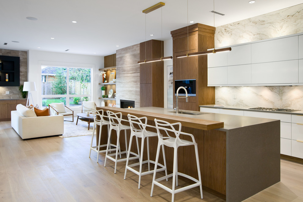 Example of a trendy galley light wood floor and beige floor open concept kitchen design in Vancouver with an undermount sink, flat-panel cabinets, white cabinets, white backsplash, stone slab backsplash, paneled appliances, an island and gray countertops