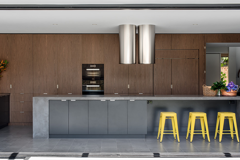 На фото: параллельная кухня в современном стиле с плоскими фасадами, темными деревянными фасадами, техникой под мебельный фасад, островом и серым полом