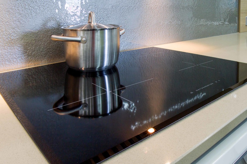 Foto på ett mellanstort funkis u-kök, med släta luckor, bänkskiva i kvarts, stänkskydd med metallisk yta och glaspanel som stänkskydd