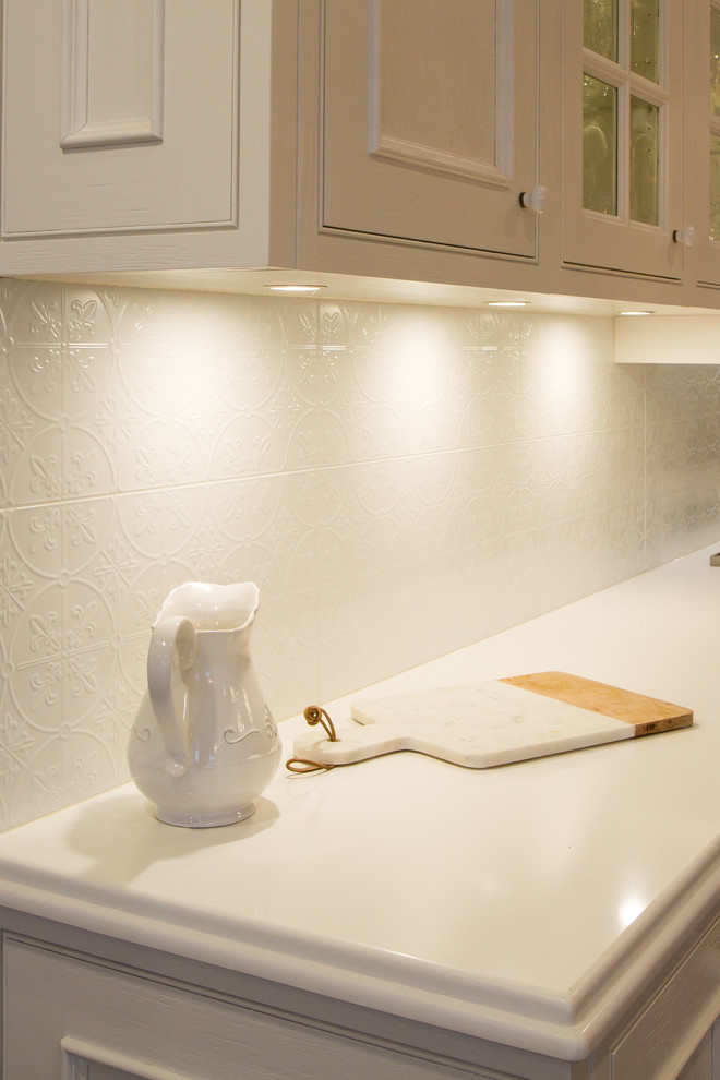 Inredning av ett klassiskt stort vit vitt kök, med en undermonterad diskho, luckor med infälld panel, vitt stänkskydd, stänkskydd i keramik, mellanmörkt trägolv, en köksö, vita skåp, marmorbänkskiva, rostfria vitvaror och brunt golv