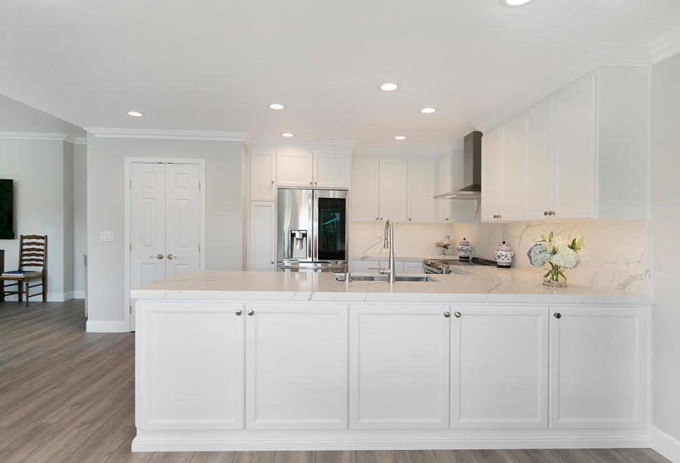Large transitional u-shaped vinyl floor and brown floor open concept kitchen photo in San Francisco with a single-bowl sink, recessed-panel cabinets, white cabinets, quartz countertops, white backsplash, stone slab backsplash, stainless steel appliances, a peninsula and white countertops