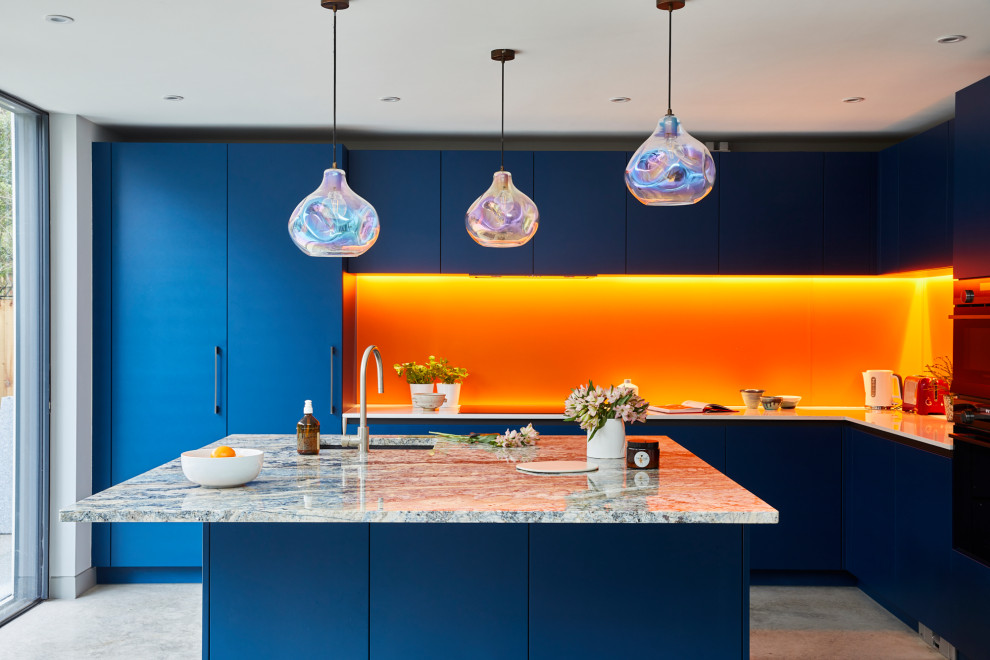 Réalisation d'une grande cuisine américaine design en L avec un placard à porte plane, des portes de placard bleues, un plan de travail en quartz, une crédence orange, une crédence en feuille de verre, un électroménager en acier inoxydable, sol en béton ciré, îlot et un sol gris.