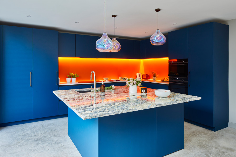 Große Moderne Wohnküche in L-Form mit flächenbündigen Schrankfronten, blauen Schränken, Quarzit-Arbeitsplatte, Küchenrückwand in Orange, Glasrückwand, Küchengeräten aus Edelstahl, Betonboden, Kücheninsel und grauem Boden in London