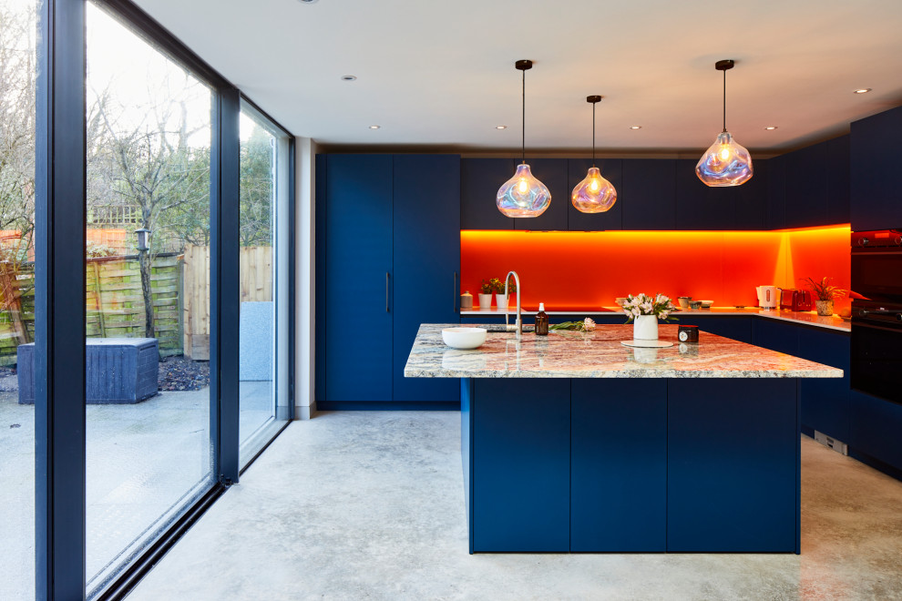 Inspiration for a large contemporary l-shaped kitchen/diner in London with flat-panel cabinets, blue cabinets, quartz worktops, orange splashback, glass sheet splashback, stainless steel appliances, concrete flooring, an island and grey floors.