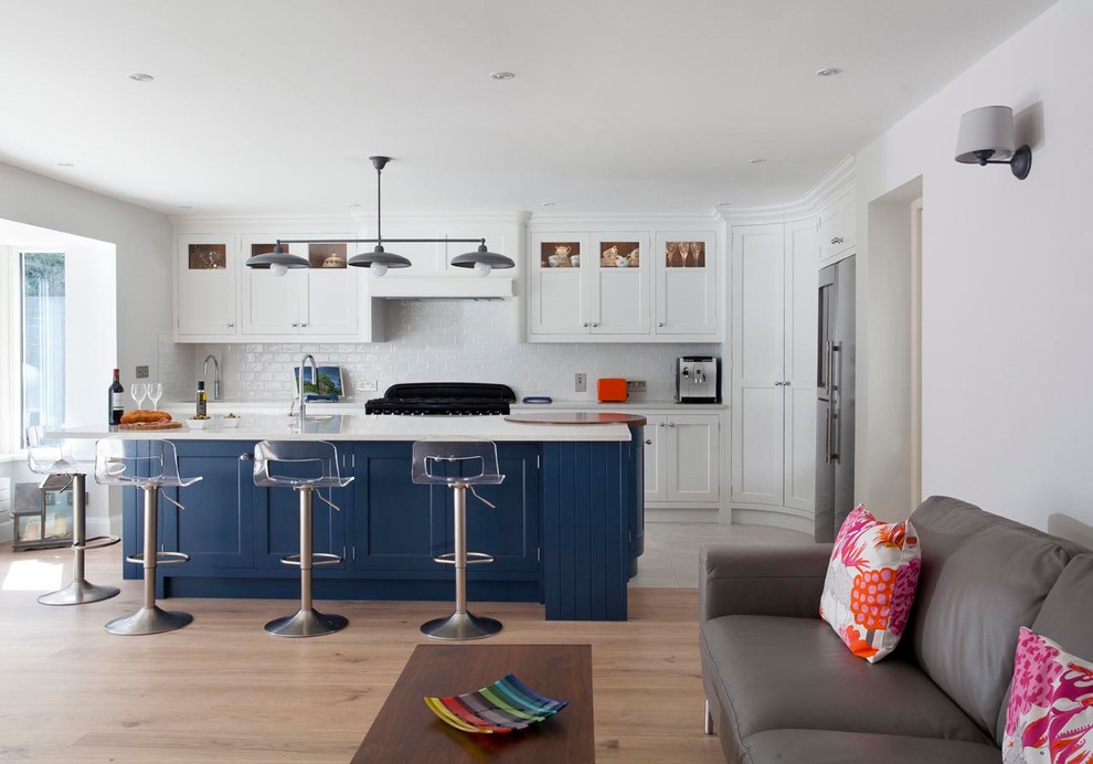 This is an example of a large traditional l-shaped open plan kitchen in Dublin with an integrated sink, shaker cabinets, blue cabinets, quartz worktops, ceramic splashback, black appliances, light hardwood flooring, an island and brown floors.