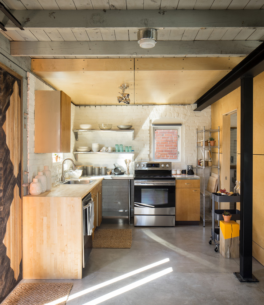 Inredning av ett industriellt litet l-kök, med träbänkskiva, rostfria vitvaror, betonggolv, en nedsänkt diskho, öppna hyllor och vitt stänkskydd
