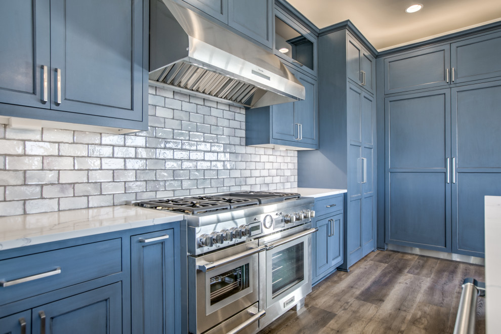 Inredning av ett klassiskt kök med öppen planlösning, med en undermonterad diskho, skåp i shakerstil, blå skåp, bänkskiva i kvarts, stänkskydd i tunnelbanekakel, rostfria vitvaror och en köksö
