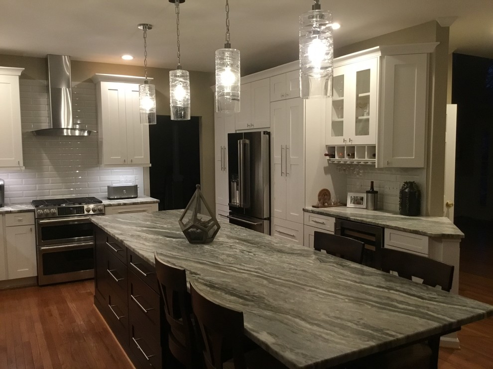 Inspiration for a mid-sized transitional u-shaped medium tone wood floor and brown floor open concept kitchen remodel in DC Metro with an undermount sink, white cabinets, granite countertops, white backsplash, subway tile backsplash, stainless steel appliances, an island, gray countertops and shaker cabinets